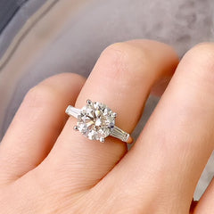 a stunningly gorgeous round center stone, set with white gold prongs on a yellow gold band, bracketed with a beautifully matched pair of tapered baguette diamonds creating an unforgettable once in a lifetime ring