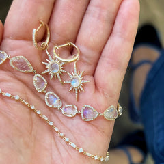 a pair of gold, diamond and rainbow moonstone earrings, and two bracelets including the confetti bracelet draped over a hand
