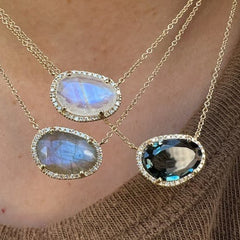 Three gold necklaces with gemstone pendants on a person wearing a brown textured garment.